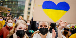 Zwei Demonstrantinnen halten ein Schild mit einem Herz in Ukraine-Farben hoch