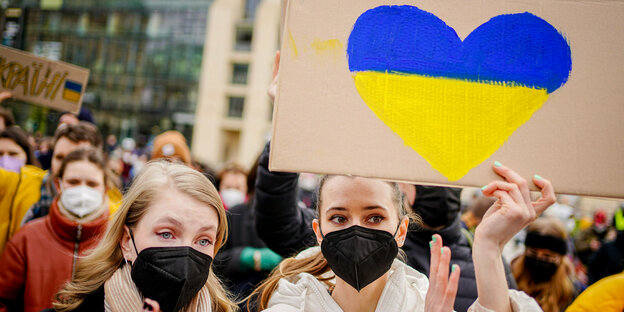 Zwei Demonstrantinnen halten ein Schild mit einem Herz in Ukraine-Farben hoch