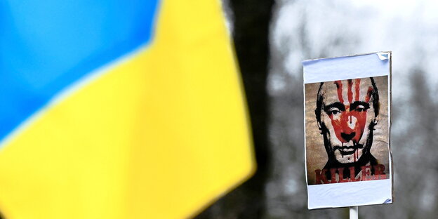 Protestakton mit ukrainischer Fahne und einem Portrait Putins auf dem mit roter Farbe "Killer" steht