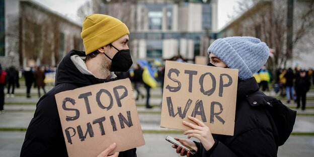 Zwei Menschen stehen vor dem Kanzleramt und fordern Stop War auf Schildern