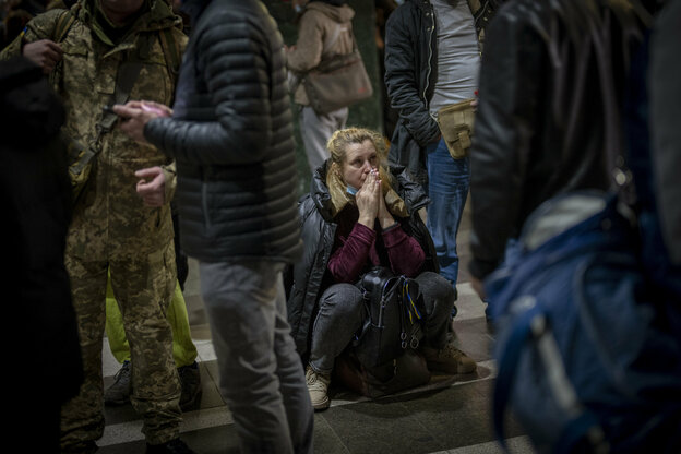 EIne weinende Frau sitzt auf einem Gepäckstück inmitten einer Menschenmenge EIne weinende Frau sitzt auf einem Gepäckstück inmitten einer Menschenmenge