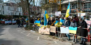 Menschen mit Flaggen der Ukraine stehen dicht gefrängt hinter Polizeiabsperrungen
