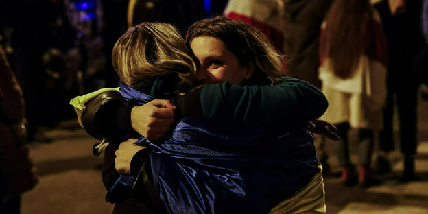 Zwei in ukrainische Fahnen gewandte Frauen umarmen sich