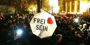 Blick von oben auf die Demonstranten vor einer Polizeikette bei einer Demonstration gegen die Corona-Maßnahmen -Zu sehen sind u.a. ein Regenschirm mit der Aufschrift - Frei sein- und ein Herz.