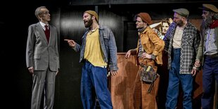 Eine Aufnahme aus dem Sting-Musical The last ship am Theater Lübeck; links steht der Werftchef im grauen Anzug, von rechts konfrontieren ihn mehrere Werftarbeiter