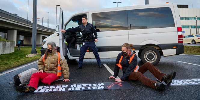 Ein Polizist und zwei Aktivist:innen vor einer Autobahnzufahrt