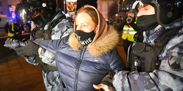 Eine Frau wird von zwei Polizisten in Kampfmontur abgeführt