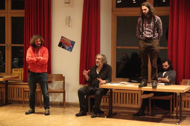 Theaterprobe: ein Mann steht auf einem Tisch, daneben sitzt einer und erklärt, ein anderer schaut stehend zu Theaterprobe: ein Mann steht auf einem Tisch, daneben sitzt einer und erklärt, ein anderer schaut stehend zu