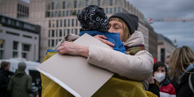 Eine Frau umarmt eine Person, die in eine ukrainische Fahne gehüllt ist.
