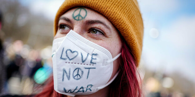 Demonstrantin mit Maske, auf der "Love Not War" steht.