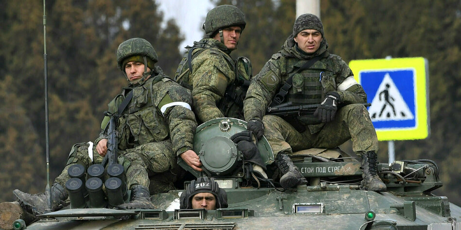 Drei bewaffnete Männer sitzen auf einem Panzer, einer schaut aus der Luke