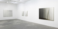 Vier Gemälde von Hyun-Sook Song hängen an zwei Wänden in der Galerie Sprüth Magers: Transparent weiße Farbbahnen überziehen die Gemälde; im Bild ganz rechts scheint unter der Farbe ein e Art Stock hervor, um dessen unteren Teil ein weißes Band gewickelt
