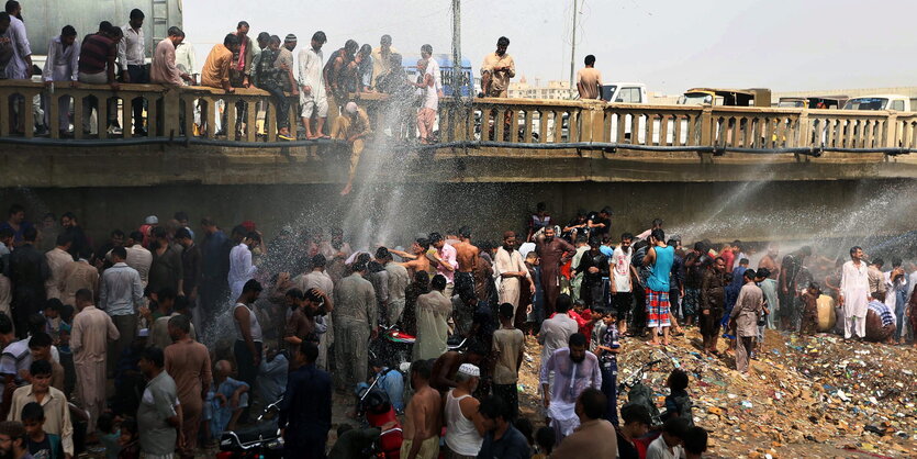 Viele Menschen sammeln sich um Wasserstrahlen aus einem beschädigten Wasserrohr, um sich abzukühlen.