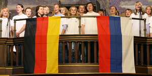 Mädchen und Jungen singen auf einer Empore, eine deutsche und russische Fahne hängt herunter