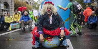 Eine Aktivistin der Klimaorganisation "Extinction Rebellion" demonstriert als Clown verkleidet auf einer Straße auf einem aufgeblasenen Erdball sitzend