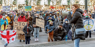 Eine Frau mit Megafon steht vor Demonstrant*innen, die Schilder mit der Aufschrift "No war" hochhalten