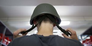 Soldat setzt seinen Helm auf, Rückenansicht