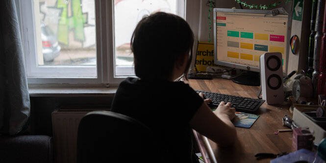 Eine Jugendliche sitzt in ihrem Zimmer am Schreibtisch vor ihrem Computer beim Homeschooling