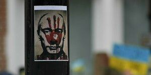 Ein Plakat hängt an einem Pfeiler mit einem Schmähplakat von Putin
