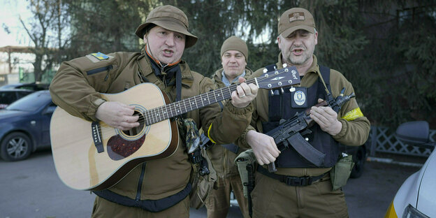 Männer mit Waffen und Gitarre singen.