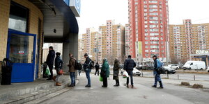 Menschen stehen in einem Hochhausviertel Schlange vor einem Supermarkt