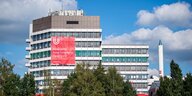 An Hochhäusern der Uni Bremen hängt ein Transparent mit den Worten "Freie Lehre, freie Forschung, freier Geist - offen seit 1971", daneben die Spitze des Fallturms