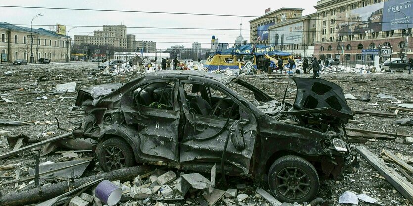 Ausgebrannte Autowracks auf einem Platz, der von Trümmern bedeckt ist