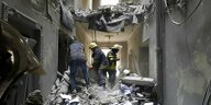 Drei Männer vom Rettungsdienst begutachten Trümmer des völlig zerstörten Rathauses