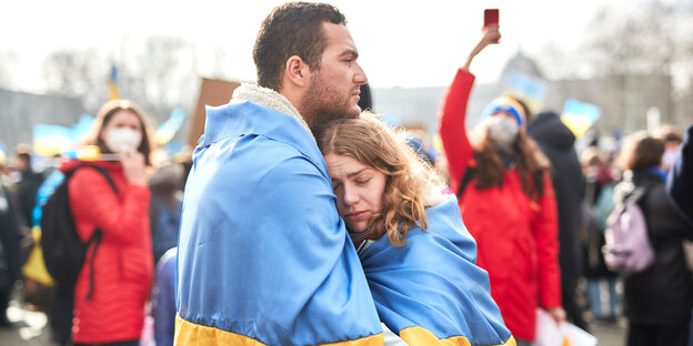 Ein Mann und eine Frau umarmen sich eingeschlungen in eine ukrainische Flagge