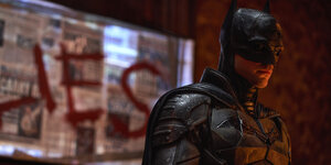 Batman mit Maske und Kostüm steht rechts im Bild, hinter ihm ist ein Fenster zugeklebt