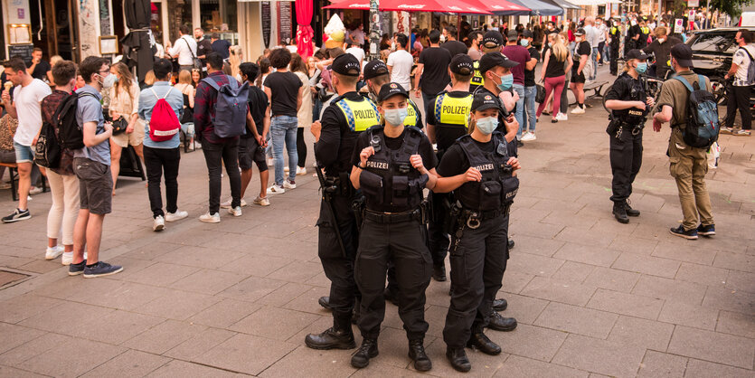 Sechs Polizist:innen stehen Rücken an Rücken auf dem Schulterblatt in Hamburg, daneben junge Leute im Freizeitmodus