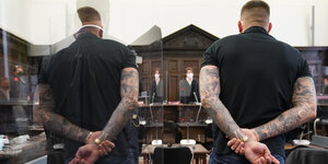 Der Rapper Gzuz, von hinten zu sehen, steht im Gerichtssaal und spiegelt sich in einer Plexiglas-Trennscheibe
