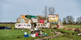 Besprühte Wohnwägen und Holzbauten auf einer matschigen Wiese.