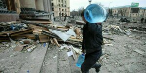 Junger Mann schleppt Wasserkanister durch zerstörte Innenstadt