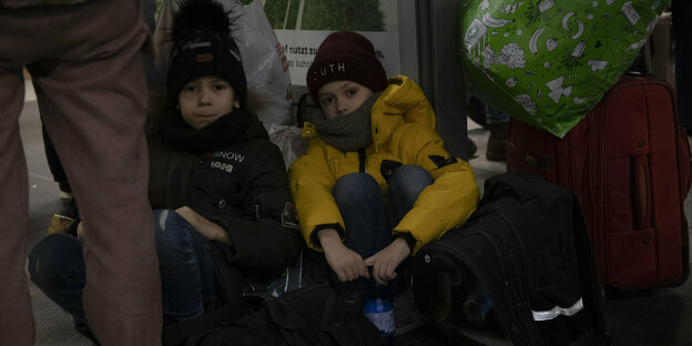 Zwei Kinder aus der Ukraine sitzen nach ihrer Ankunft am Berliner Hauptbahnhof in einer Ecke auf dem Boden