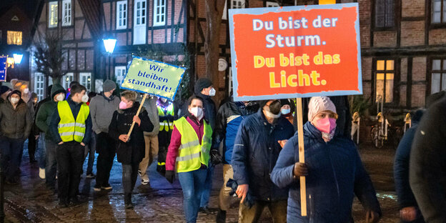 Menschen mit Atemschutzmasken gehen durchd ie Verdener Altstadt mit Schilder, auf denen steht: "Du bist der Sturm, du bist das Licht" oder "Wir bleiben standhaft"