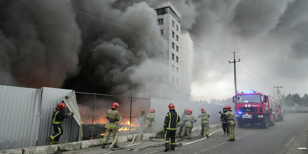 Feuerwehrleute mit Löschwagen stehen vor einem brennenden Gebäude