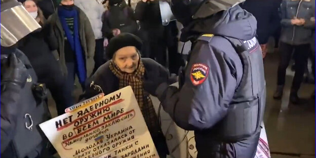 Eine ältere Frau mitz zwei Plakaten in der Hand wird von zwei Polizisten mit Helm abgeführt Eine ältere Frau mitz zwei Plakaten in der Hand wird von zwei Polizisten mit Helm abgeführt