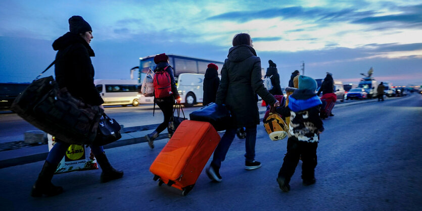 Frauen und Kinder mit Rollkoffern gehen eine Straße entlang