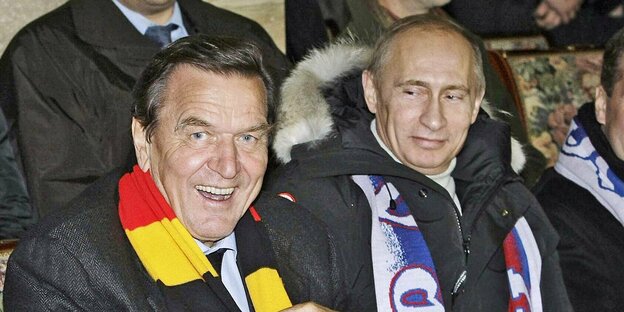 Mit Fußballschals sitzen grinsend Gerhard Schröder und Wladimir Putin auf einer Tribüne