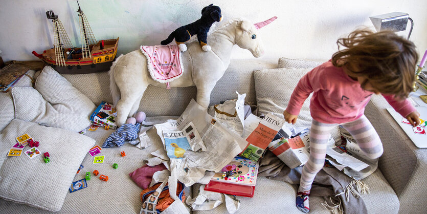 Zwei Kinder spielen zwischen zerrissenen Zeitungen auf dem Sofa