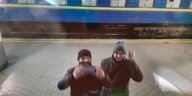 Zwei Männer stehen an einem Bahnhof und winken
