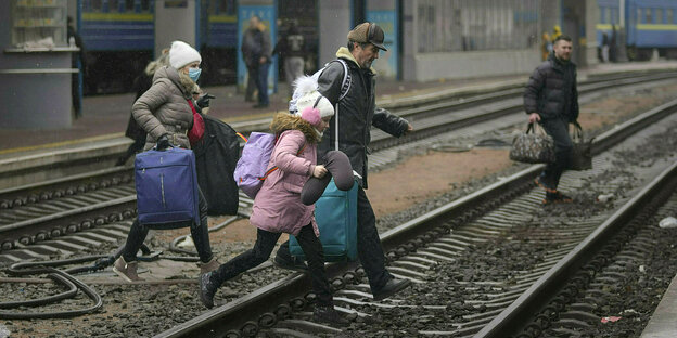 Eine Familie spurtet über die Gleise eines Bahnhofs