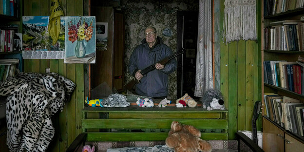 Ein älterer Mann steht entschlossen mit seinem Gewehr in seinem Schlafzimmer
