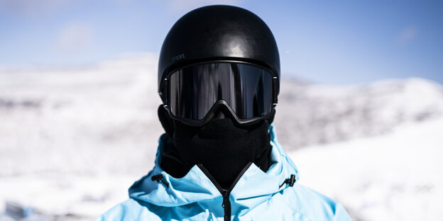 Ein schawarzer Helm bedeckt einen Menschen vor einer Schneekulisse