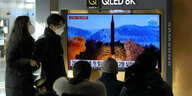 Passanten beobachten Fernsehbilder eines Raketenstarts an einem Bildschirm in einem Bahnhof.