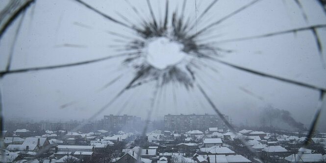 Schussloch in einem Fensterglas mit Blick auf die Stadt Mariupol, die seit Tagen von russischen Truppen angegriffen wird