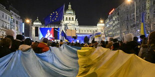 Eine ukrainische Flagge wird von einer Gruppe Demonstranten in einer nächtlichen Menschenmenge getragen.