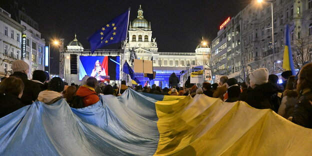 Eine ukrainische Flagge wird von einer Gruppe Demonstranten in einer nächtlichen Menschenmenge getragen.