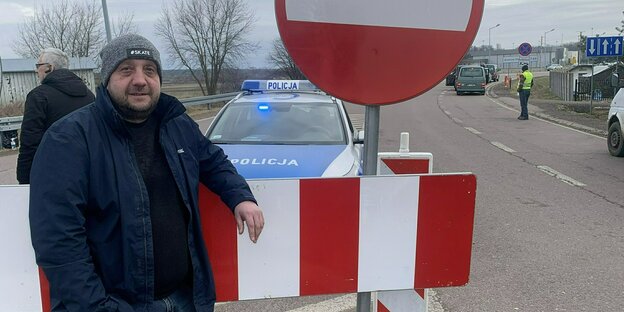 Ein Mann steht an einem Stopp-Schild auf einer Straße und blickt in die Kamera Ein Mann steht an einem Stopp-Schild auf einer Straße und blickt in die Kamera